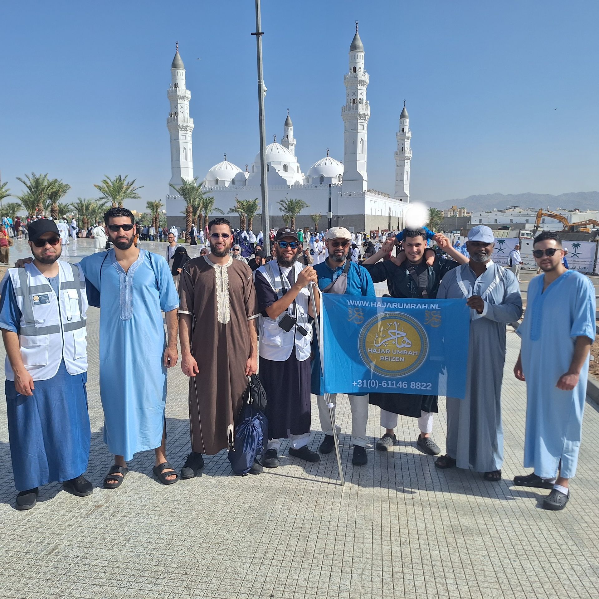 Een groep mannen die voor een moskee staan ​​en een blauwe vlag vasthouden