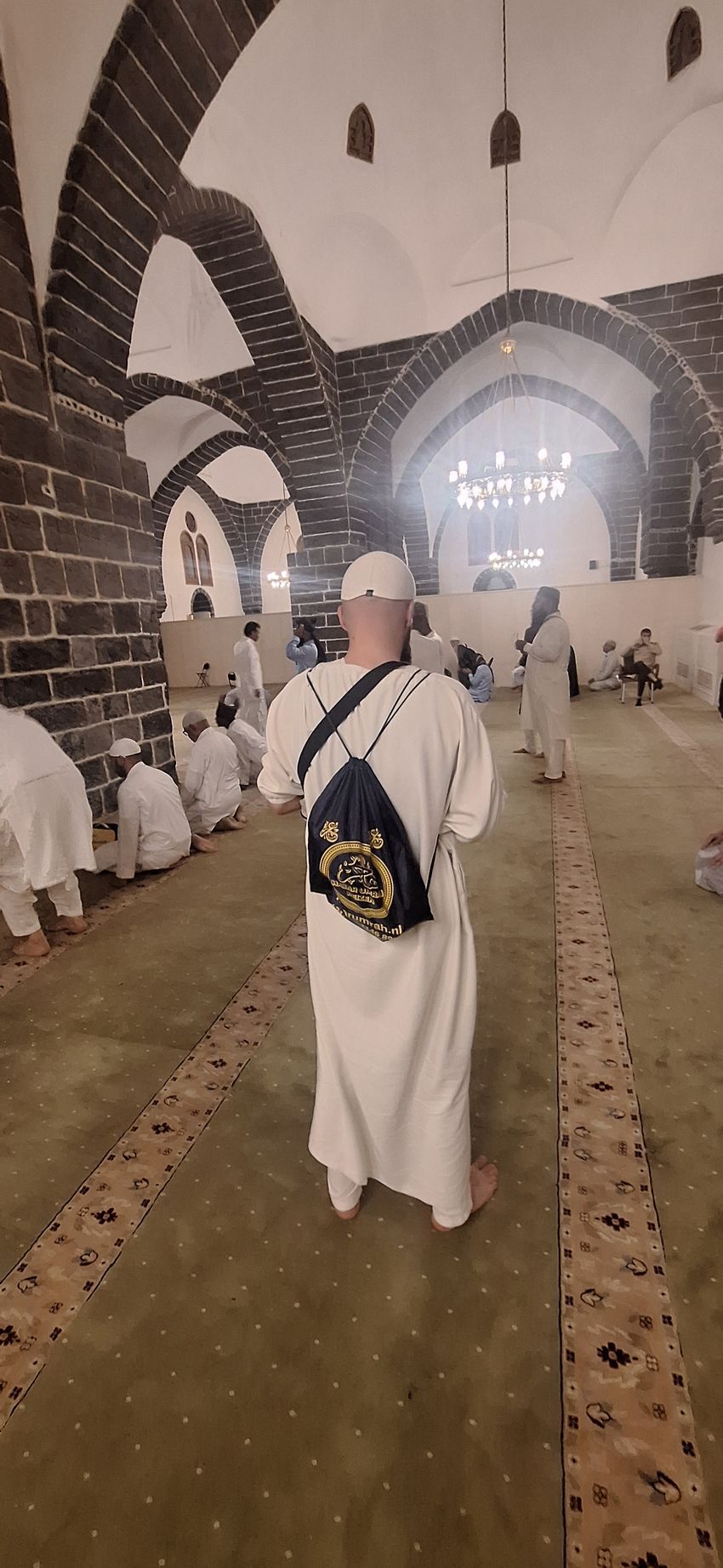 Een man staat in een moskee met een rugzak op zijn rug.