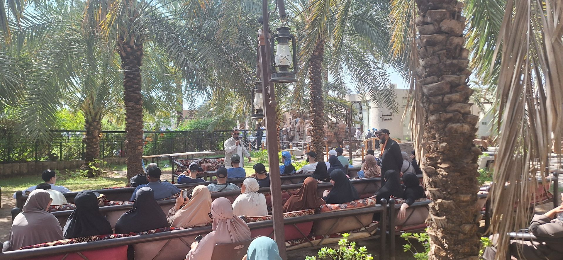 Een groep mensen zit aan tafels in een park.