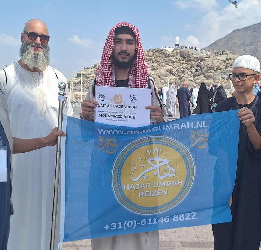 Een groep mannen die een blauwe vlag vasthouden met de tekst hajar umrah reizen