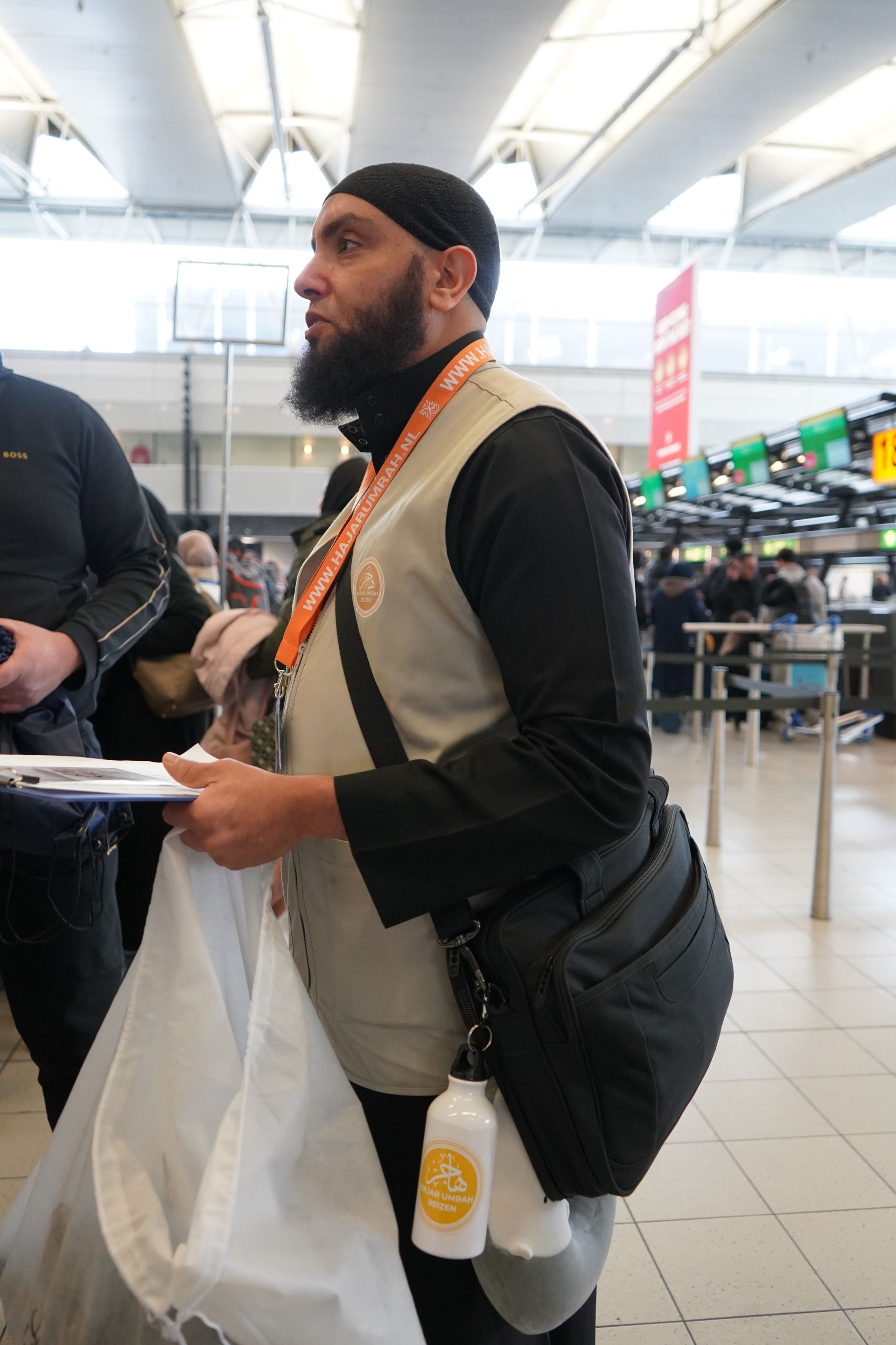 Een man met een baard staat op een luchthaven met een tas in zijn handen