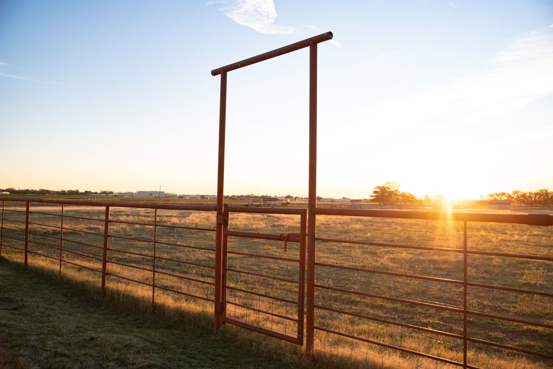 a fence with a gate in the middle of a field at sunset .