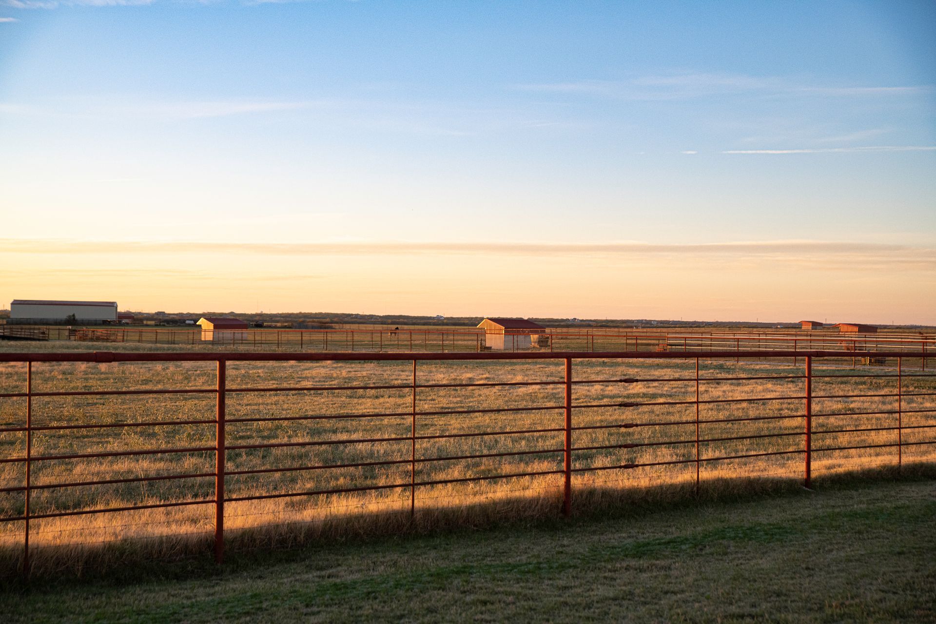 a red fence surrounds a field with a sunset in the background .