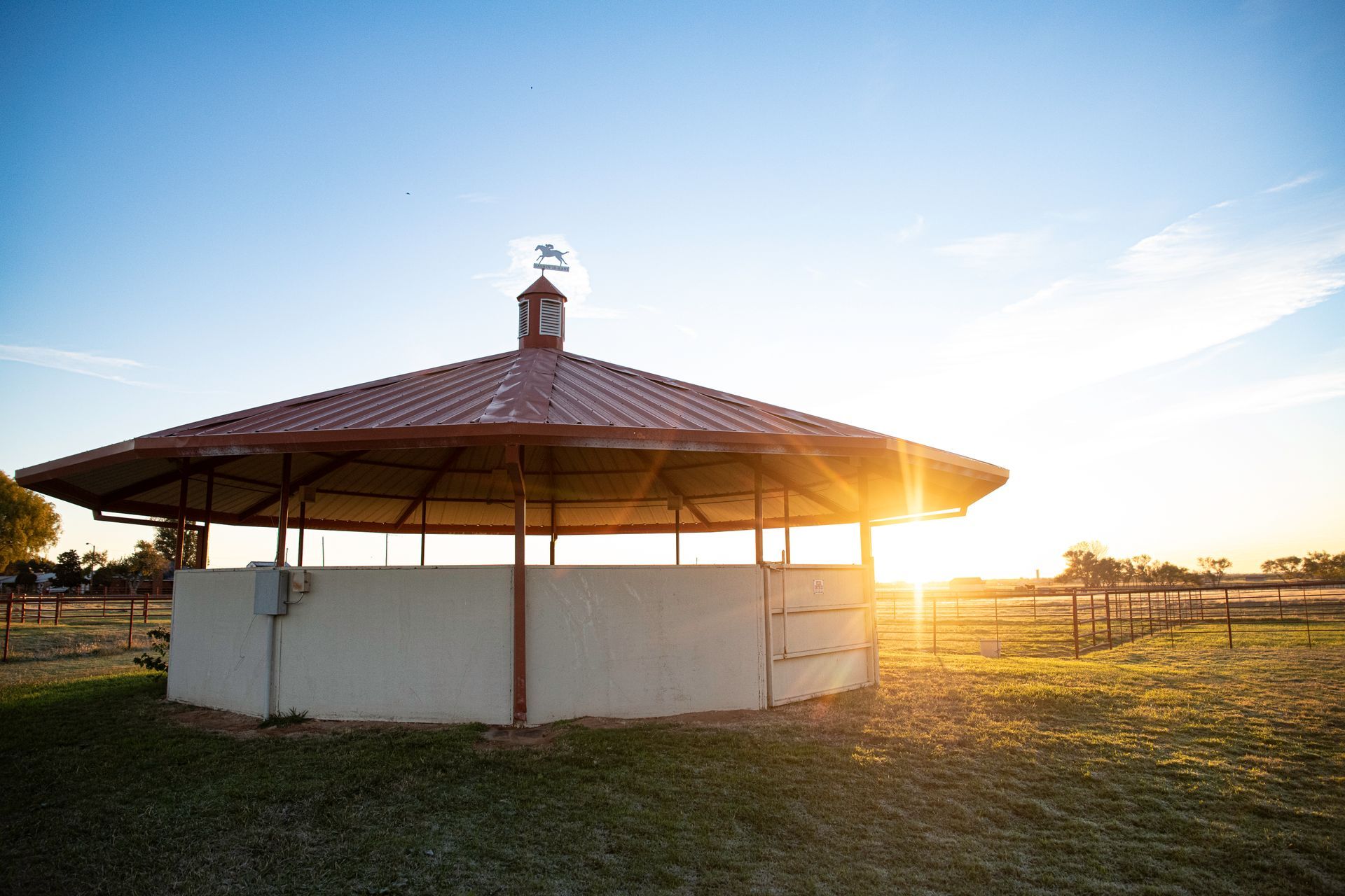 a round building with a red roof is in the middle of a grassy field .