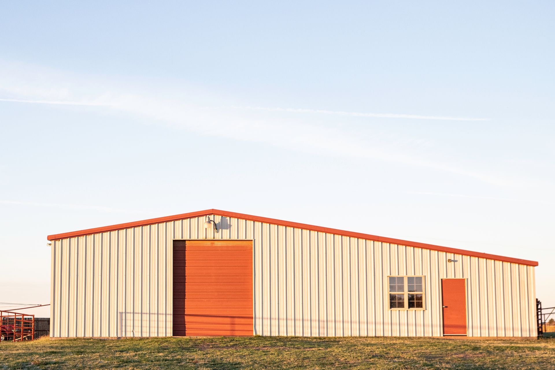 a large metal building with a red door is sitting in the middle of a grassy field .