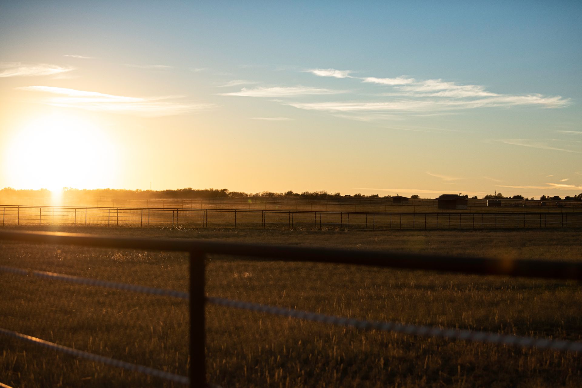 the sun is setting over a field with a fence in the foreground .