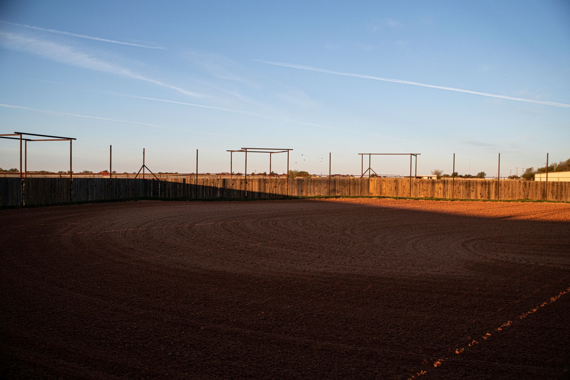 a dirt field with a fence around it and a blue sky in the background .