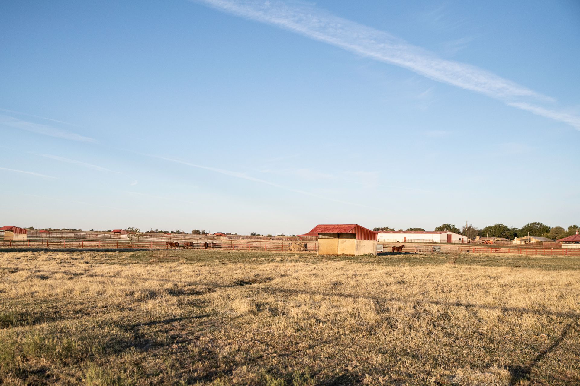 a large dry grass field with a fence in the foreground and a building in the background .