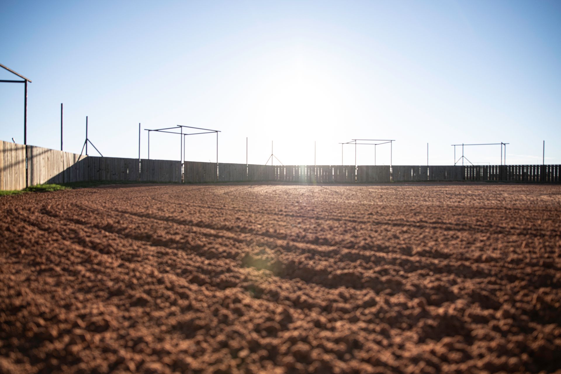 the sun is shining through the fence of a dirt field .