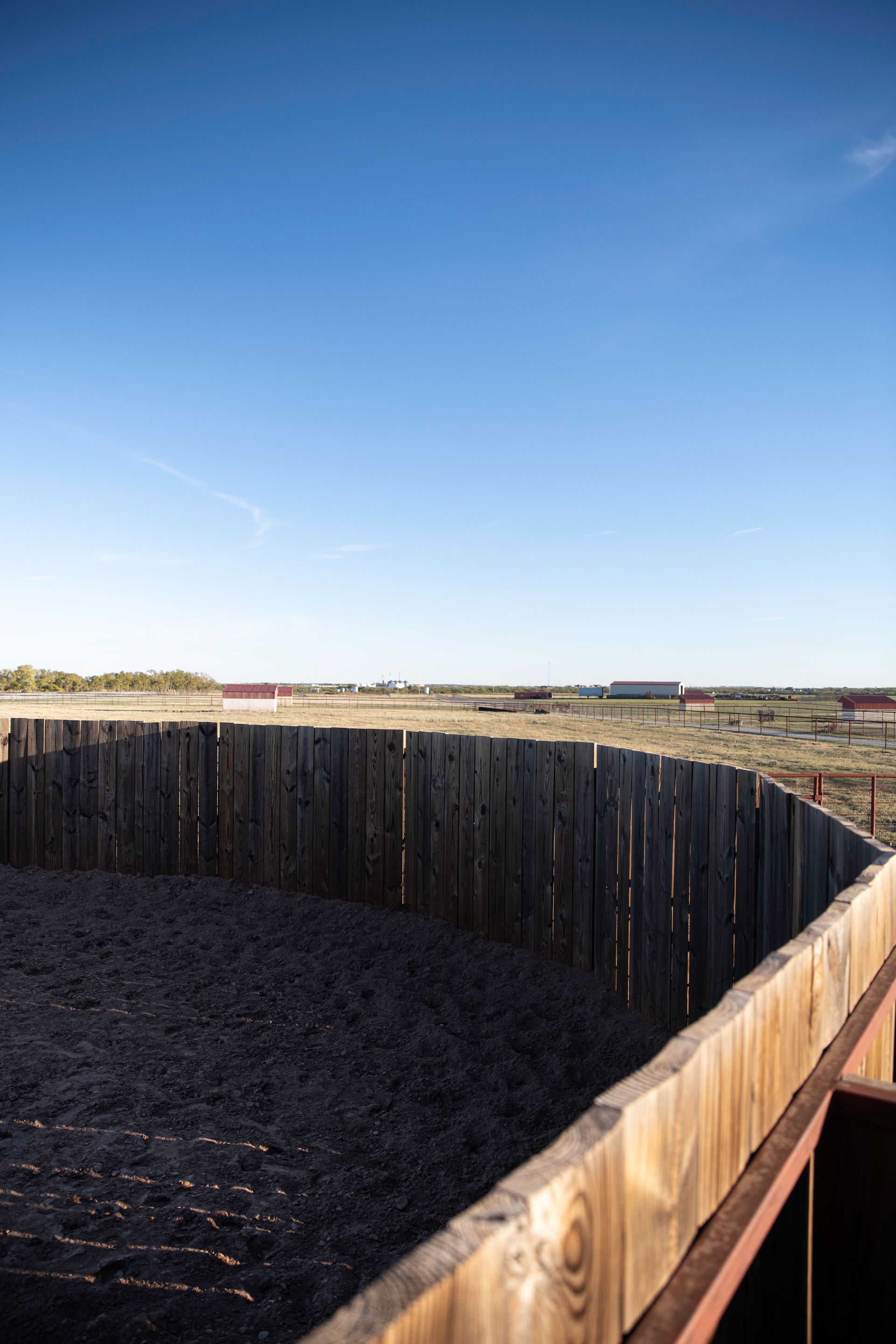 a wooden fence surrounds a dirt field with a blue sky in the background .