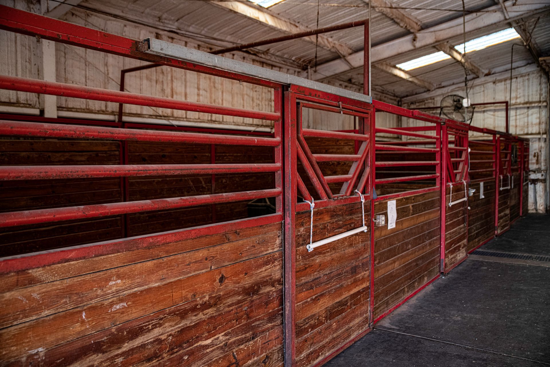 a row of wooden stables with red metal bars in a barn .