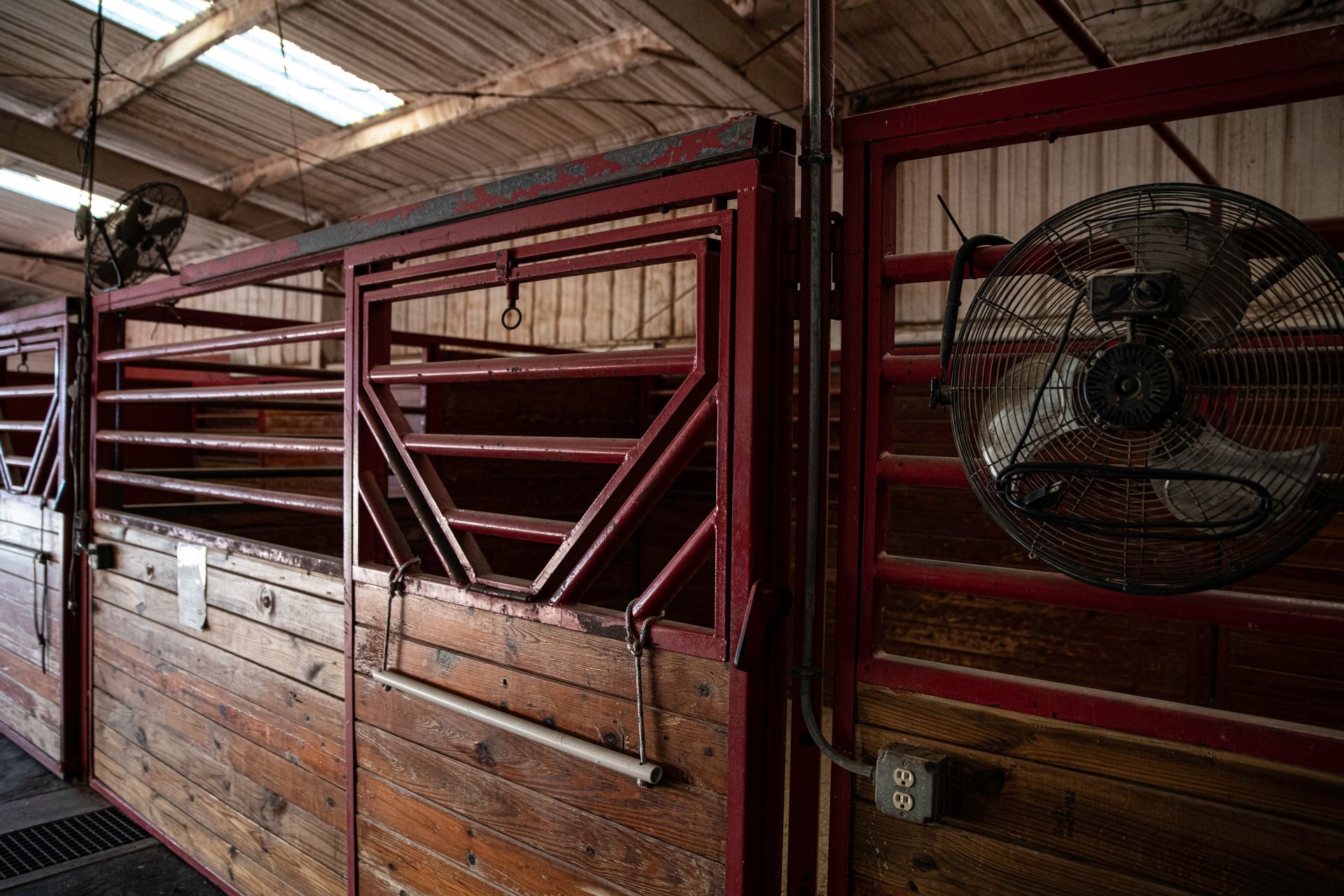 a row of wooden stables with fans hanging from the ceiling .