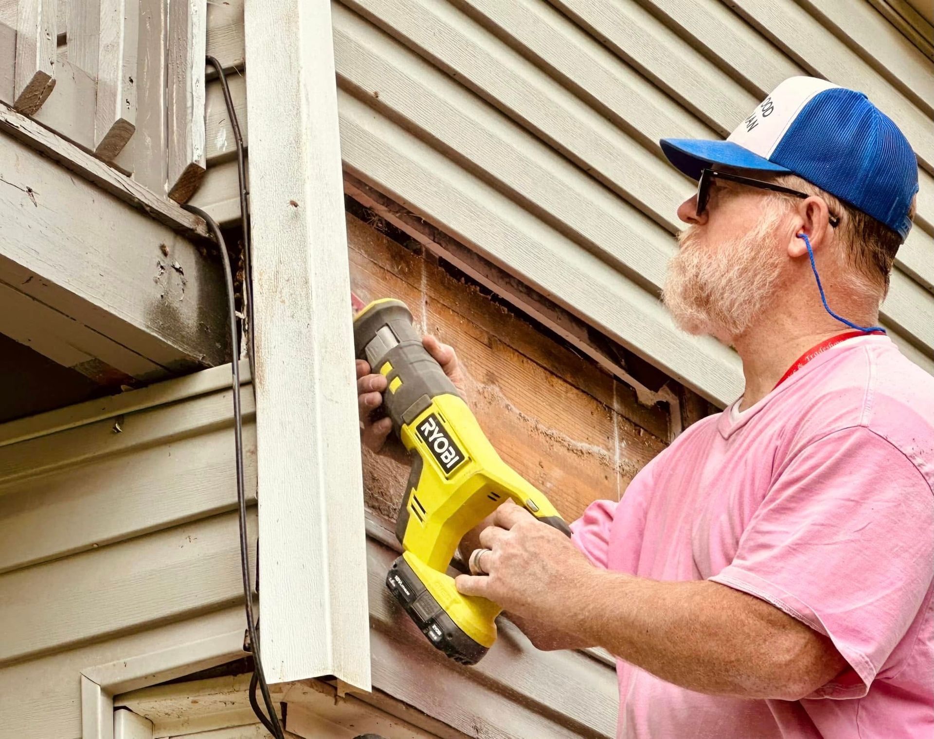 Person in pink shirt using a yellow power tool to work on outdoor house siding