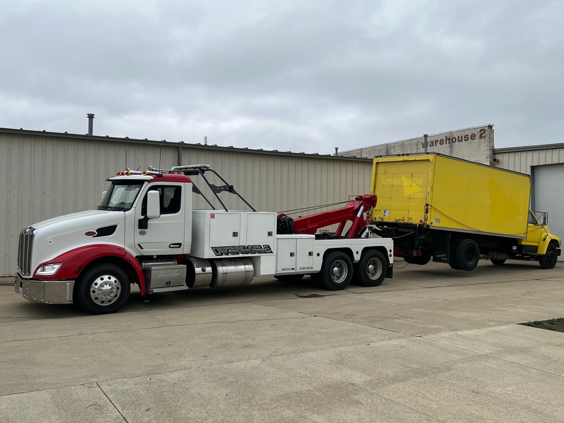 A white and red tow truck is towing a yellow truck.