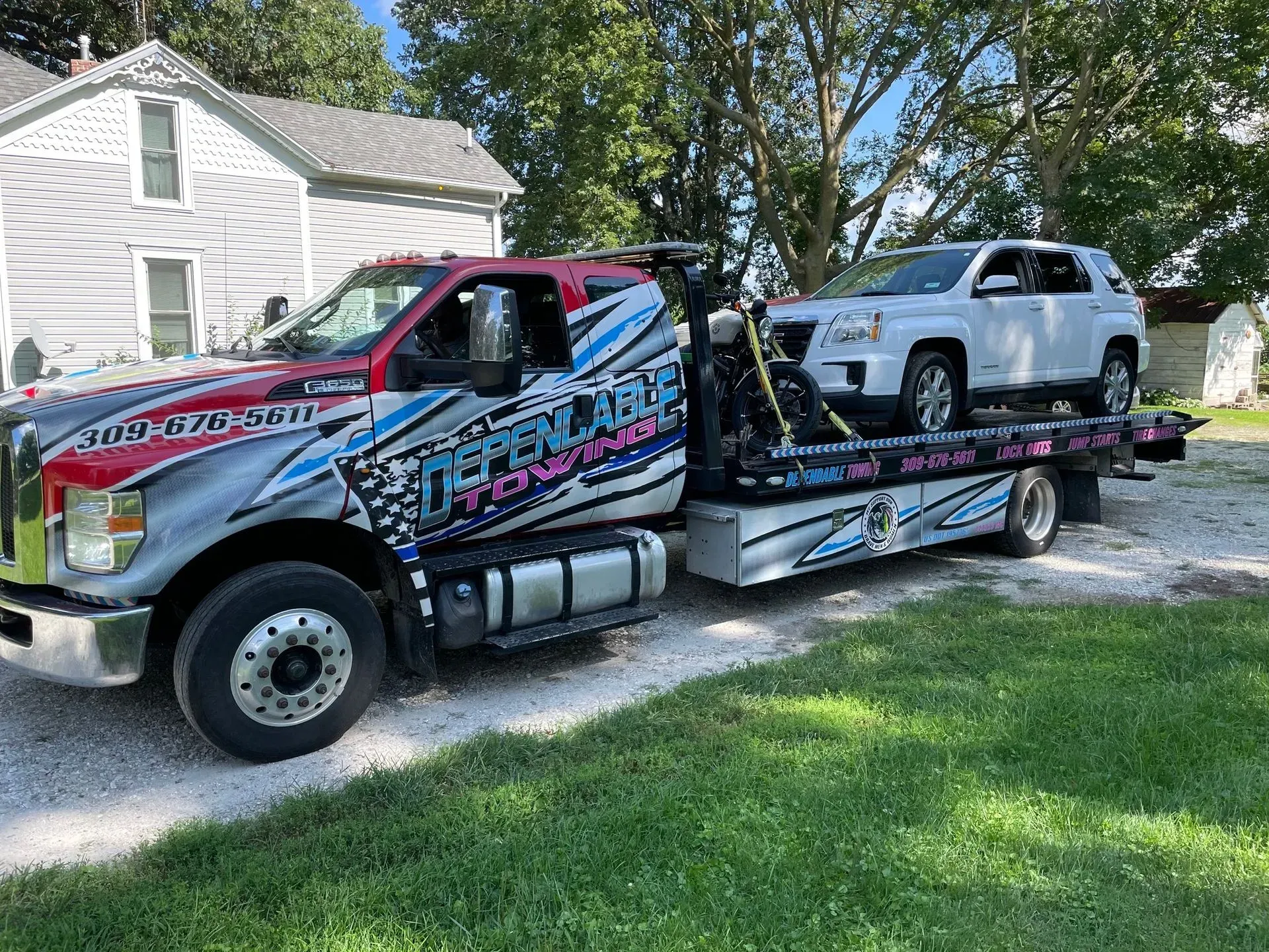 A tow truck is towing a white suv in front of a house.