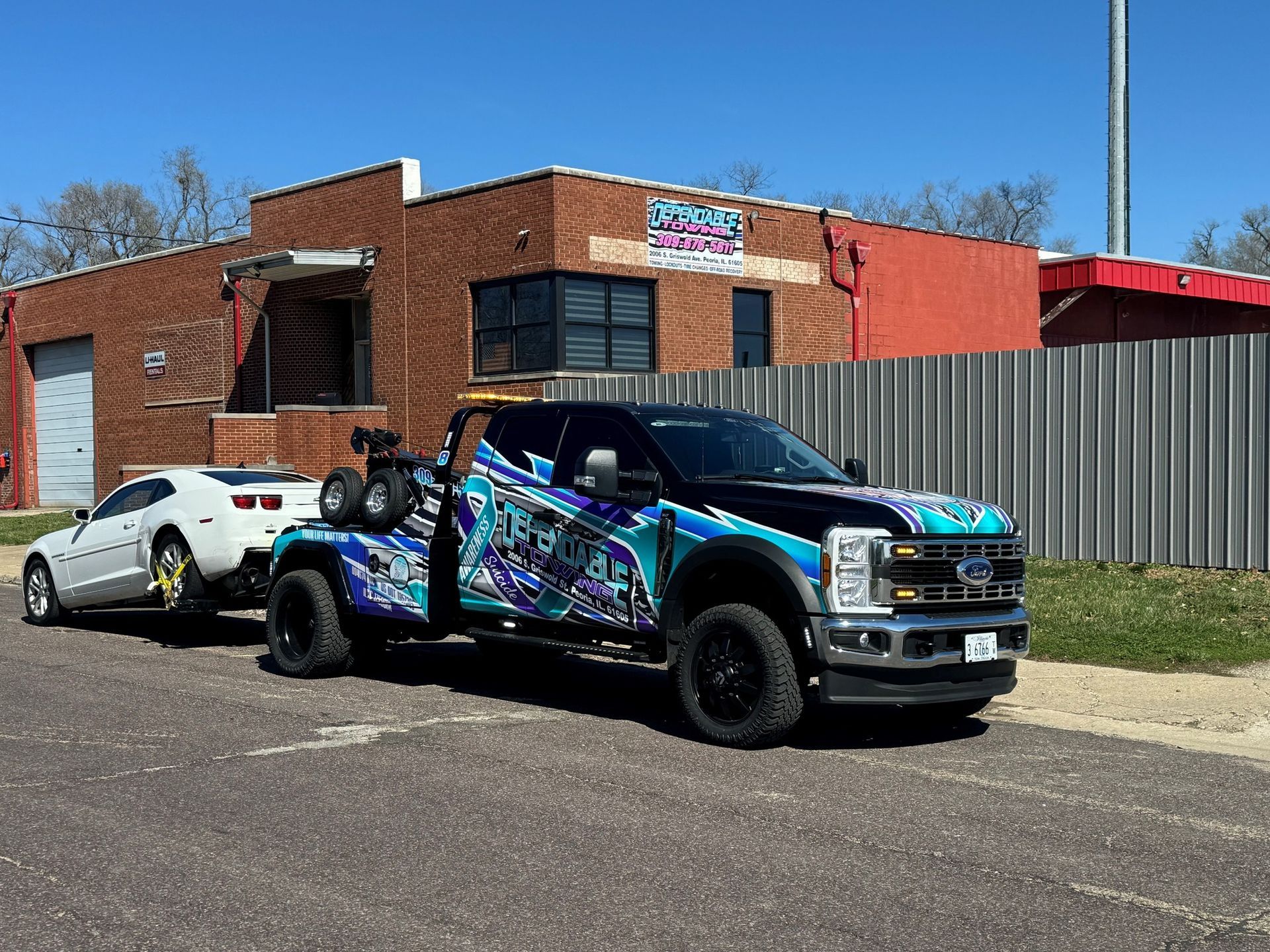 A tow truck is towing a white car down a street.
