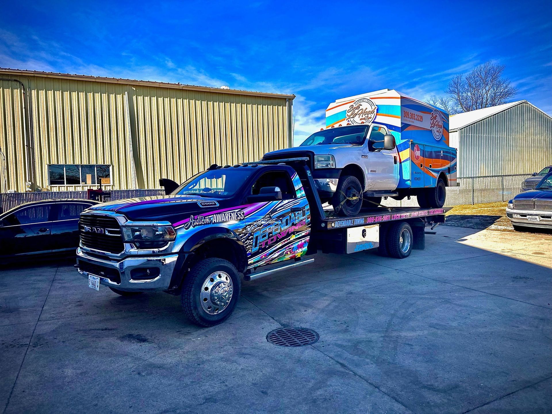 A tow truck is carrying a blue ambulance on the back of it.