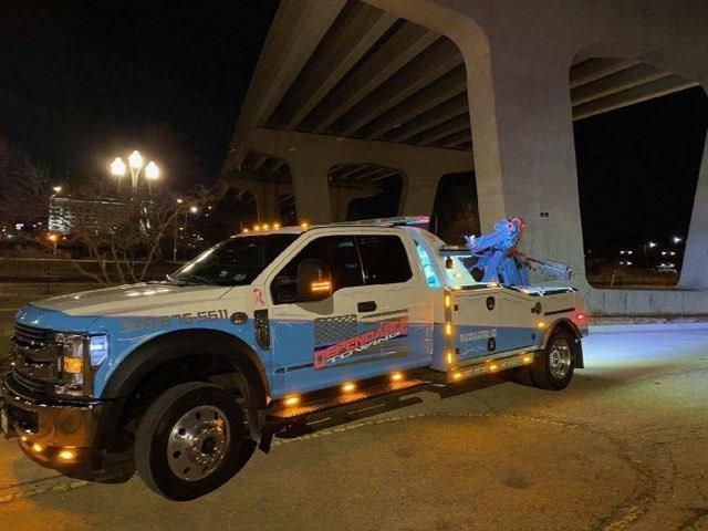 A blue and white tow truck is parked under a bridge at night.