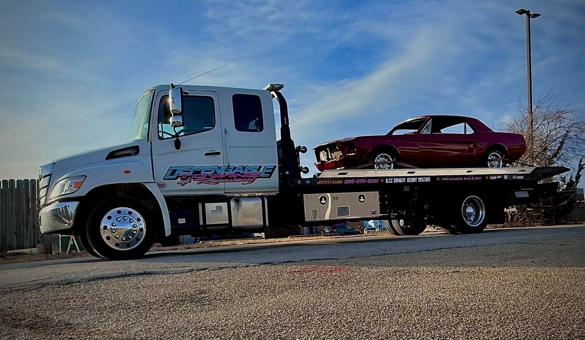 A tow truck with a red car on the back is parked on the side of the road.