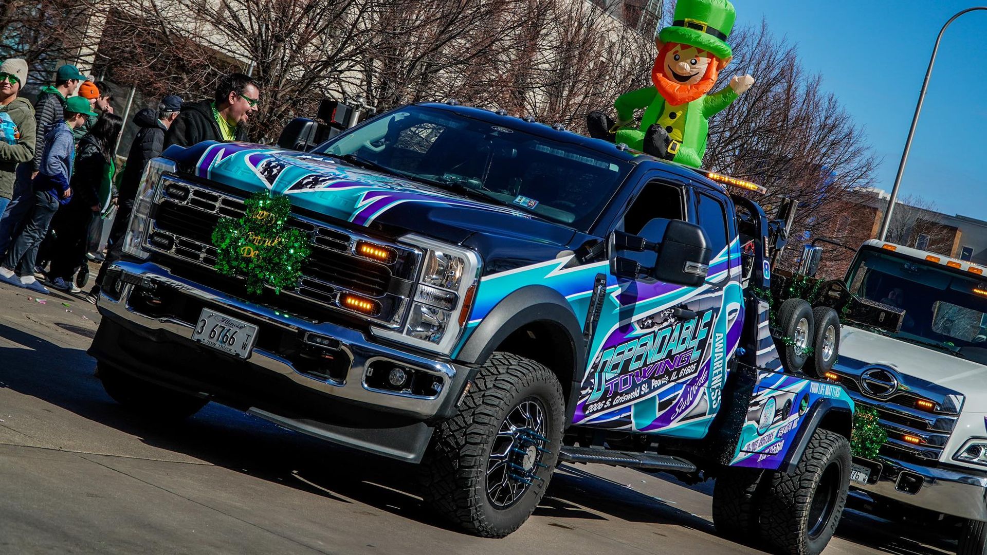 A truck with a leprechaun on top of it is driving down the street.