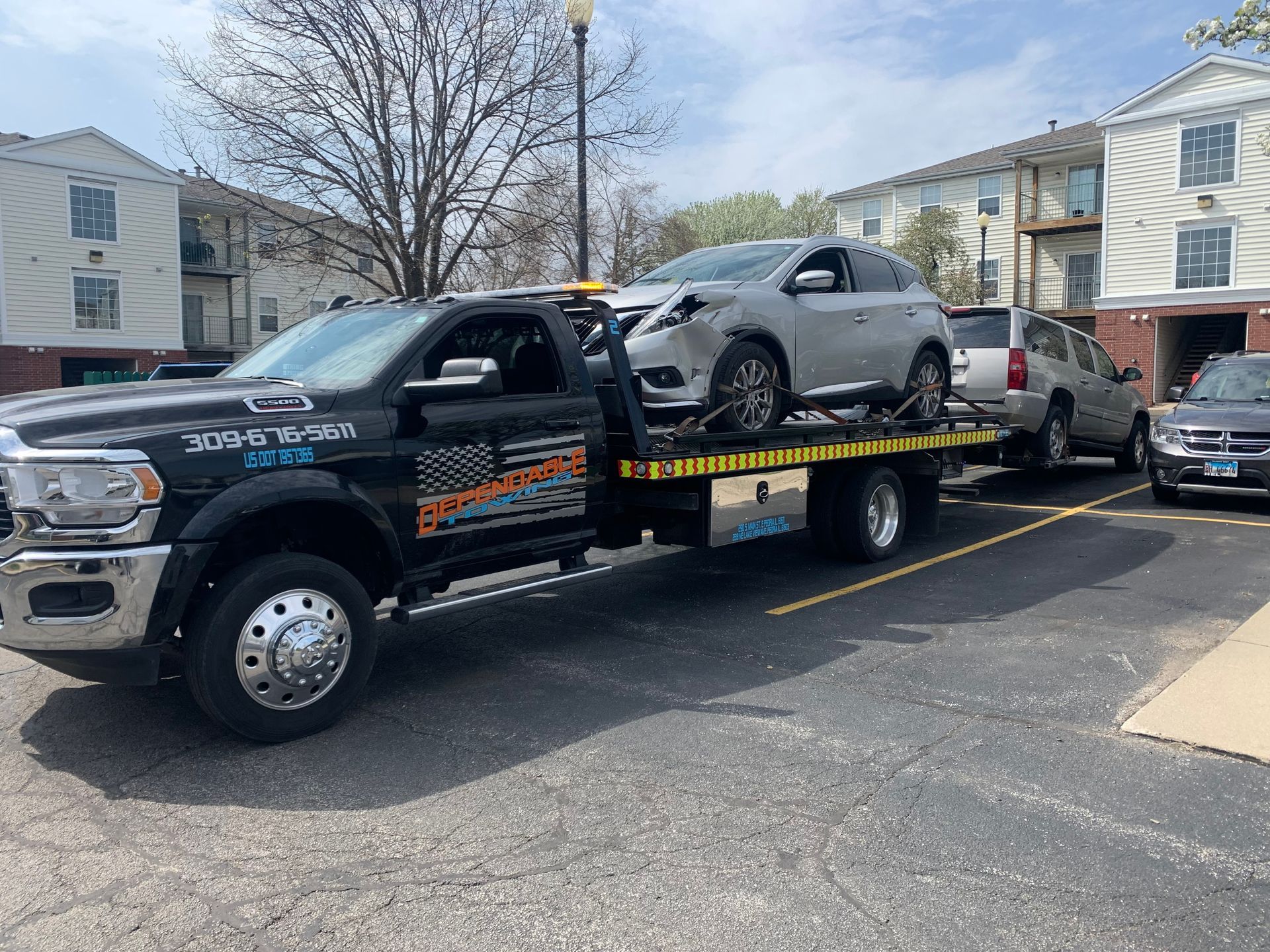 A tow truck is towing two cars in a parking lot.