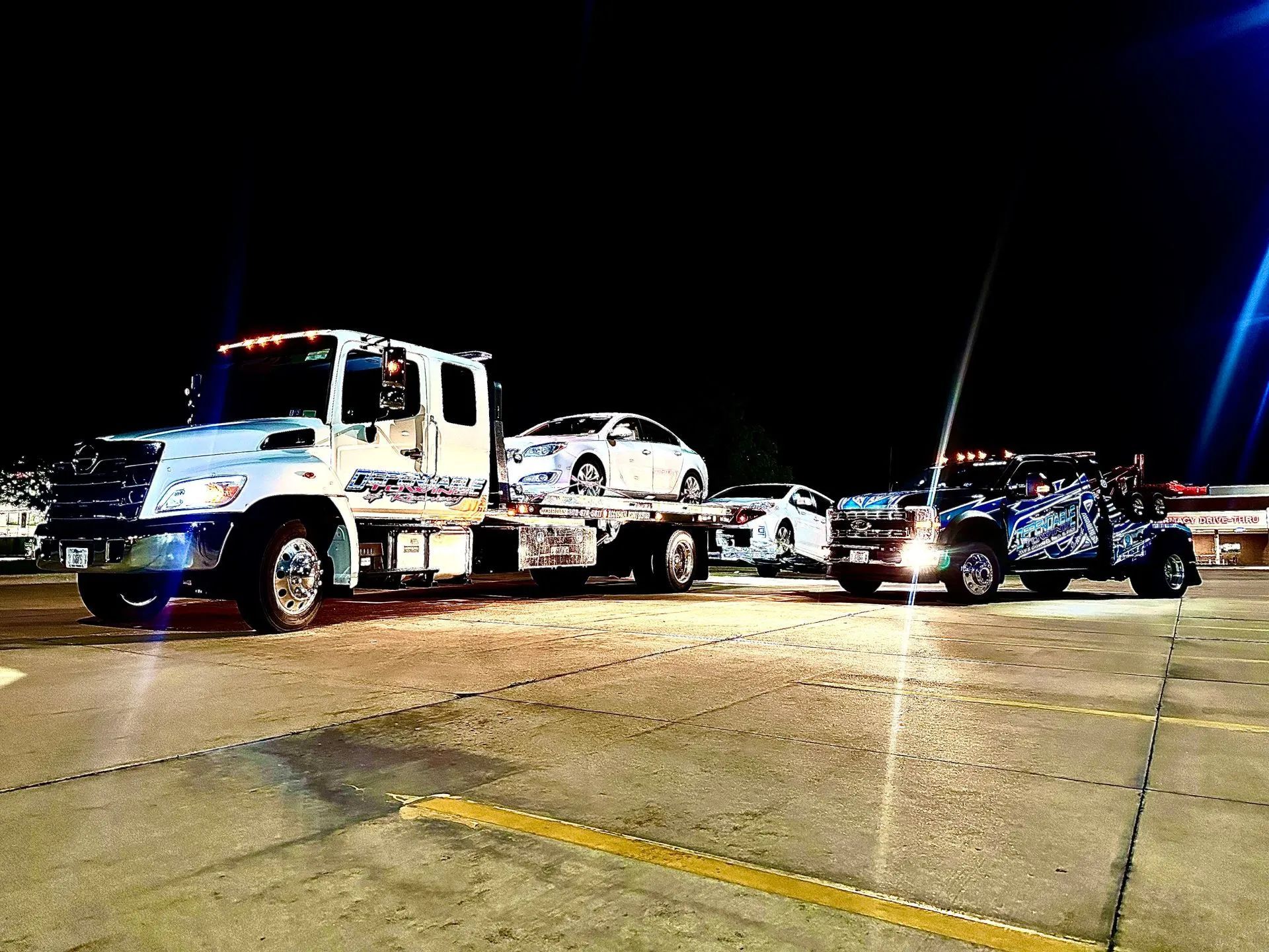 Two tow trucks hauling cars at night.