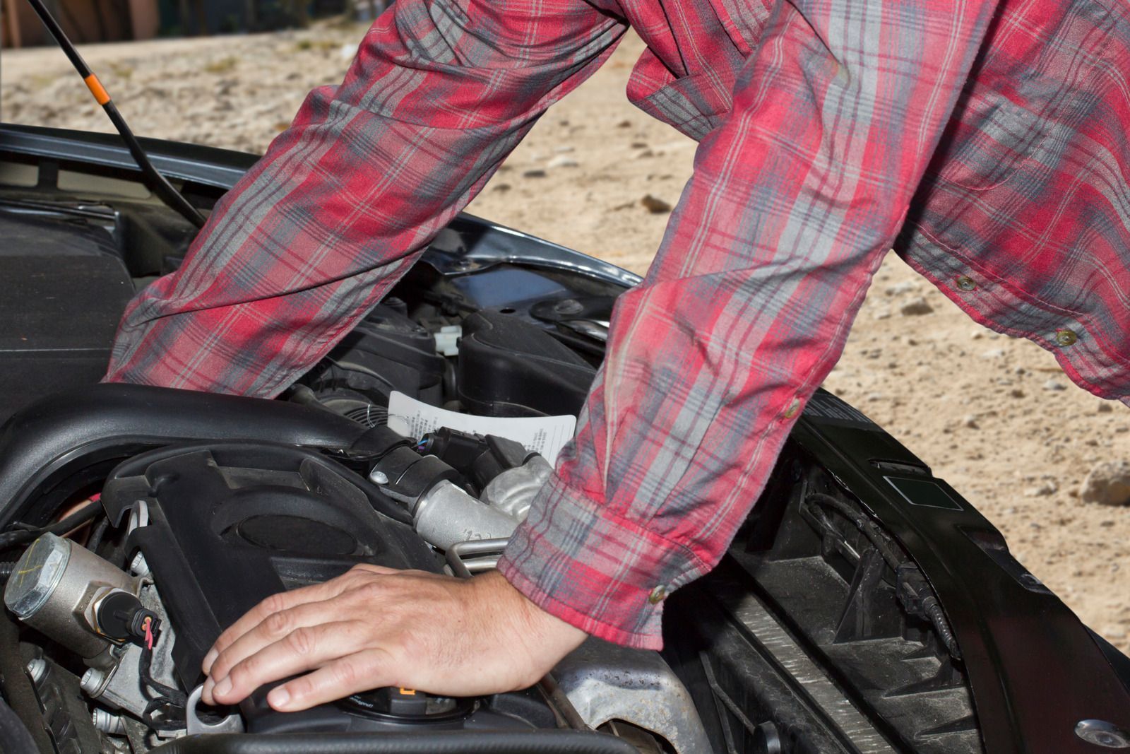 A man in a plaid shirt is working on the engine of a car.