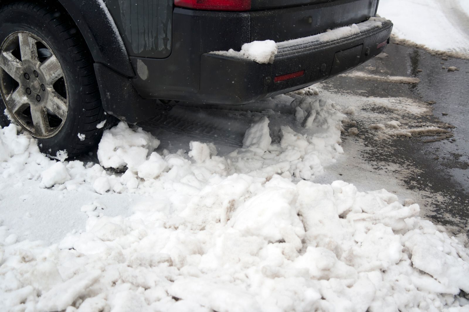 A black car stuck in a pile of snow on a snowy road.