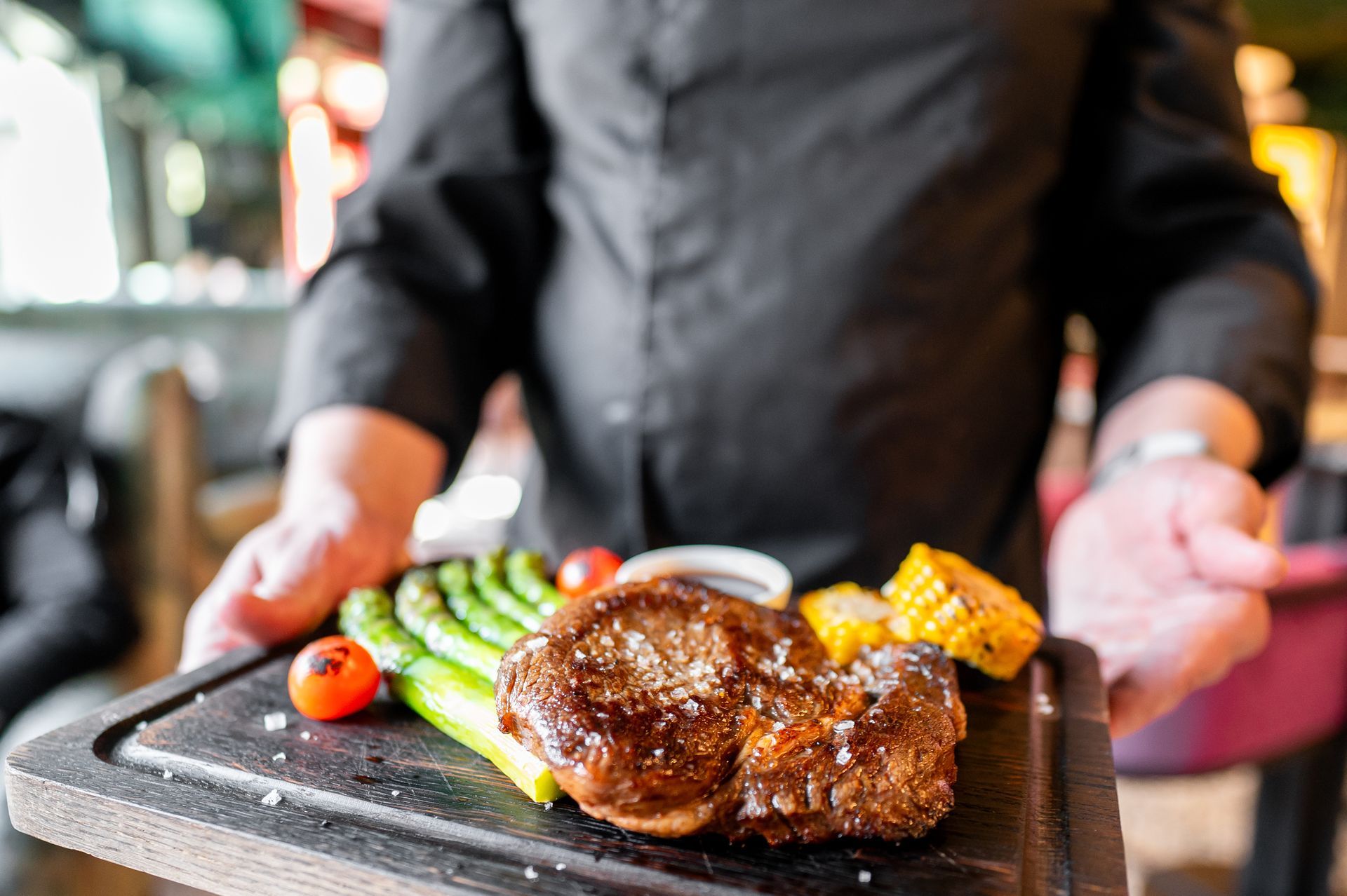 A man is holding a plate of food with a steak and vegetables on it.