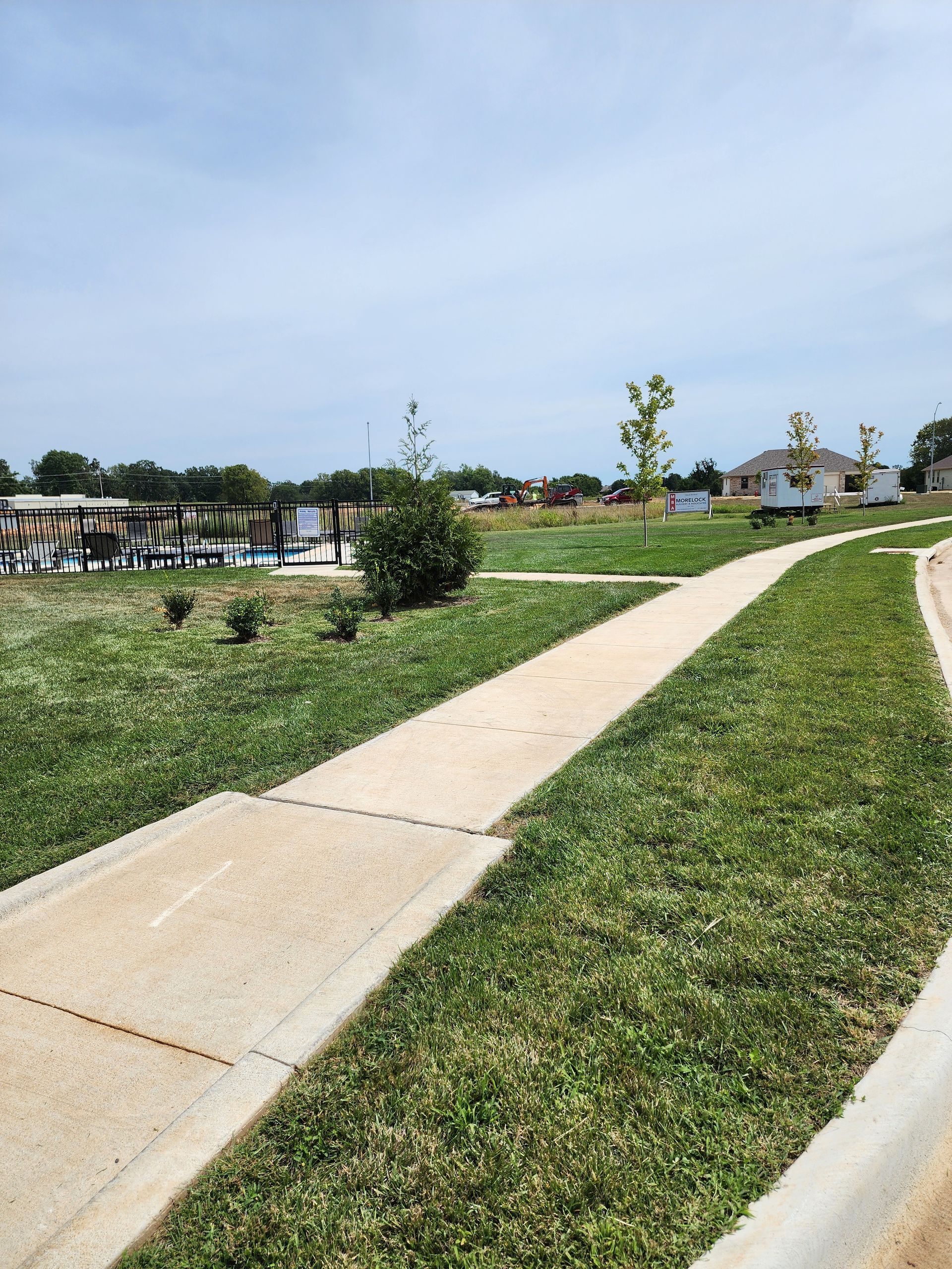 A sidewalk going through a grassy field with a house in the background.