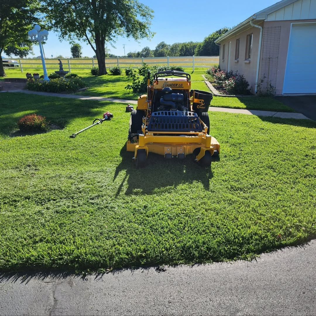A yellow lawn mower is parked in the grass in front of a house.