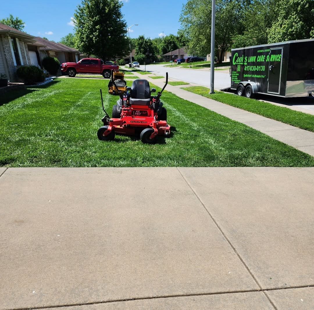 A red lawn mower is parked in the grass next to a trailer.