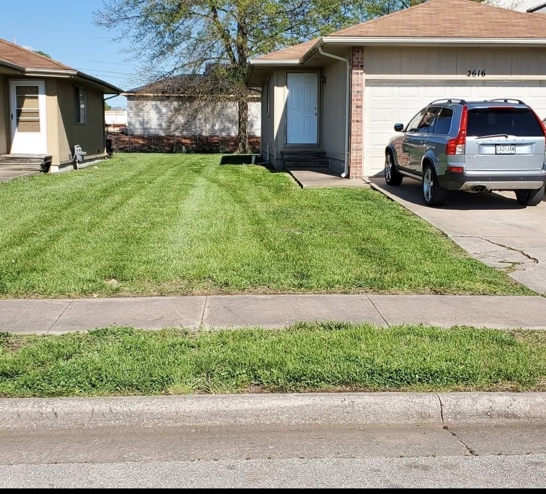 A car is parked in front of a house with a lush green lawn