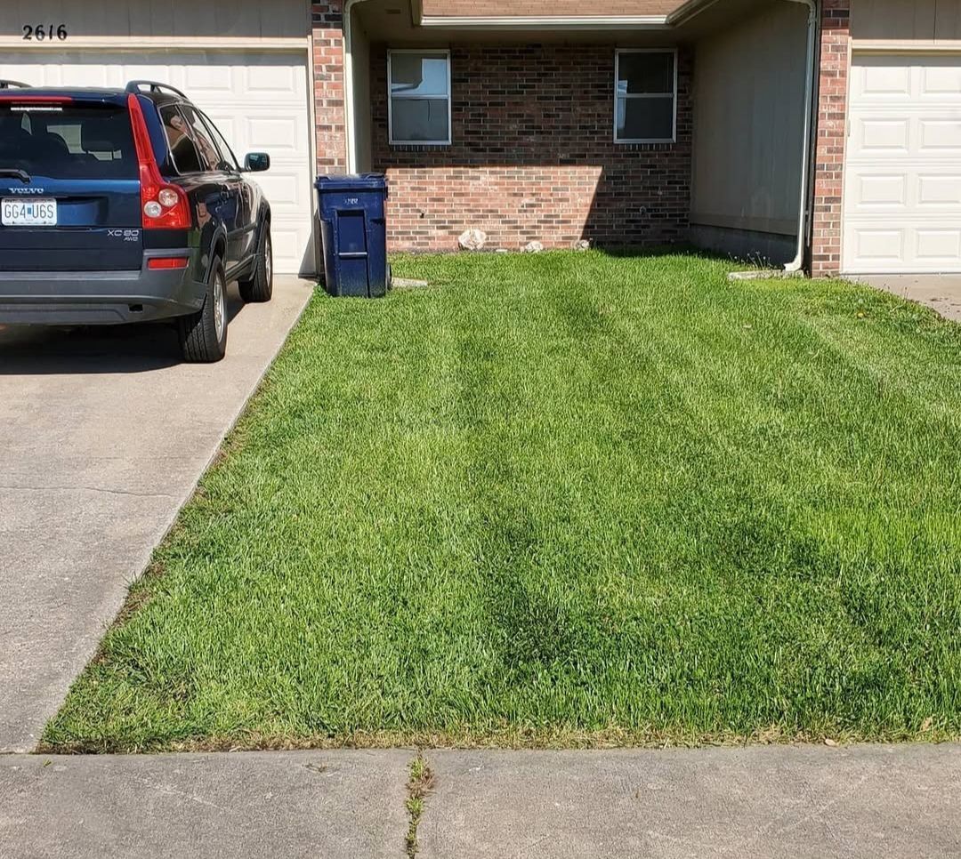 A car is parked in front of a house with a lush green lawn.
