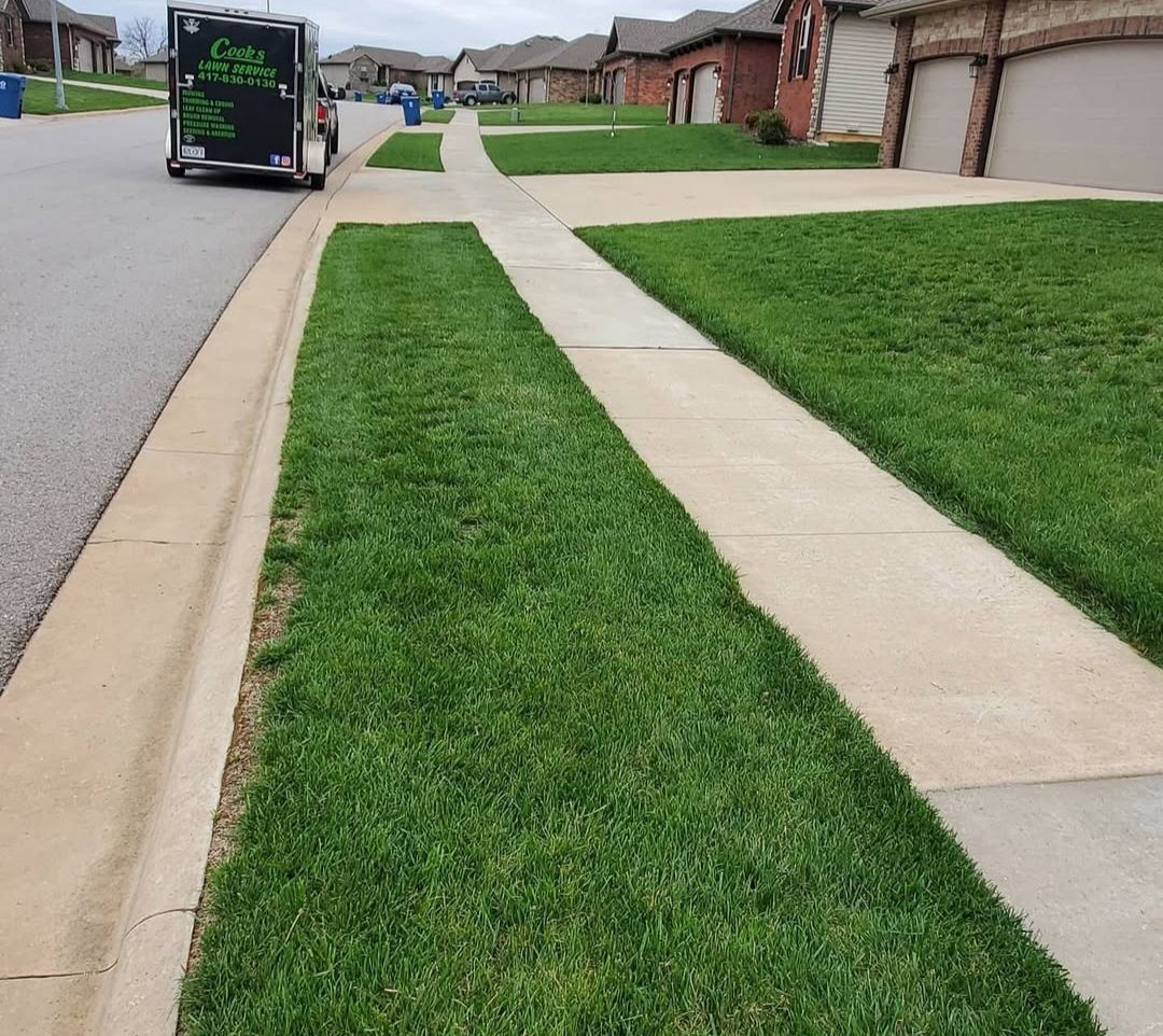 A trailer is parked on the side of the road next to a lush green lawn.