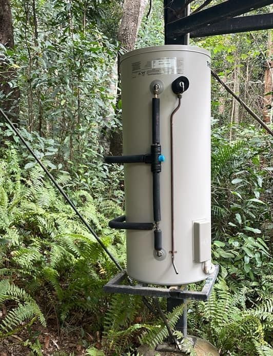 A White Water Heater Is Sitting In The Middle Of A Forest — Russell Plumbing In Cairns, QLD