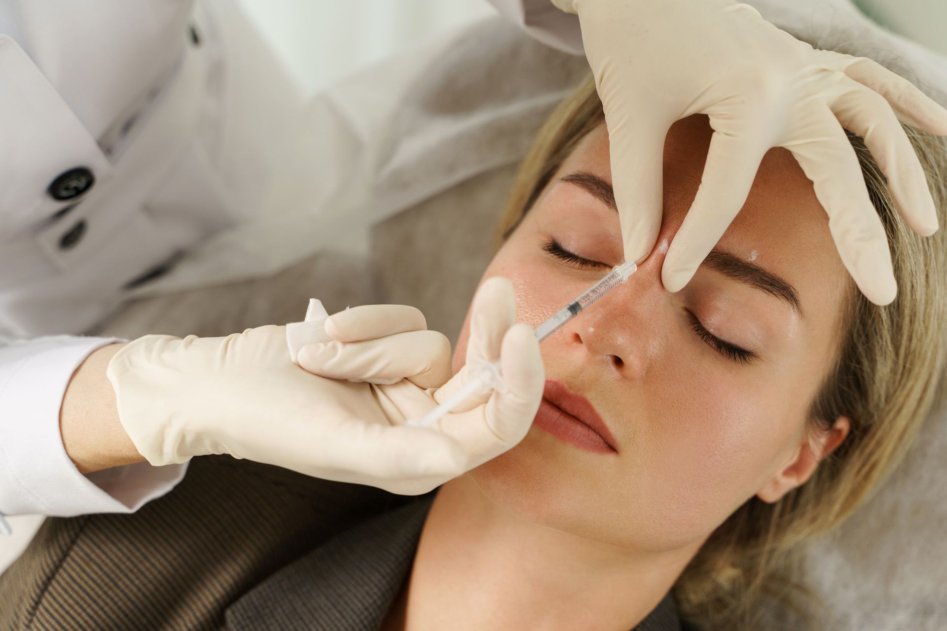 Woman receiving a nose injection by a person wearing gloves in a medical setting.