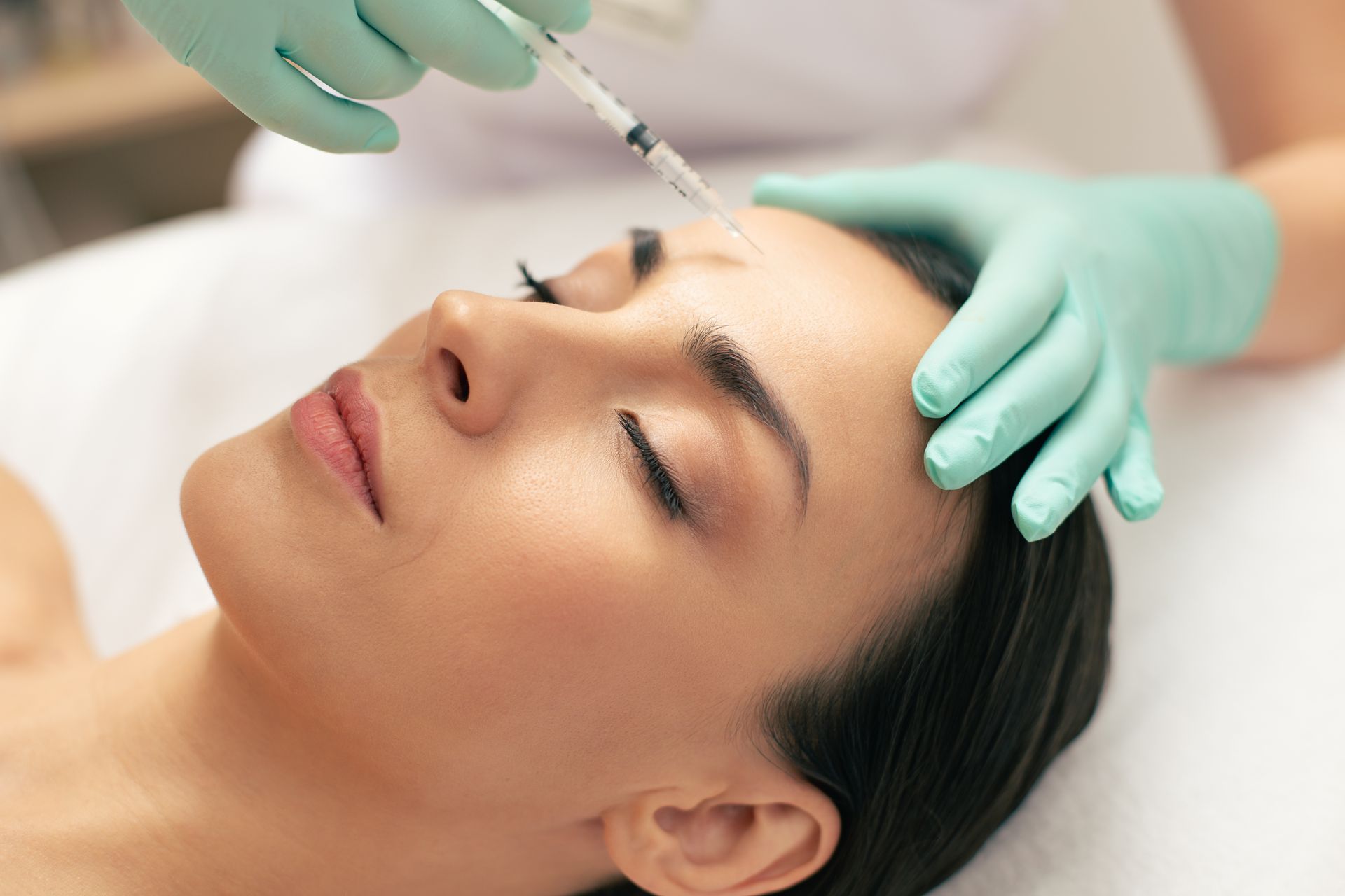 Woman receiving a facial injection on her forehead, eyes closed, in a beauty clinic.