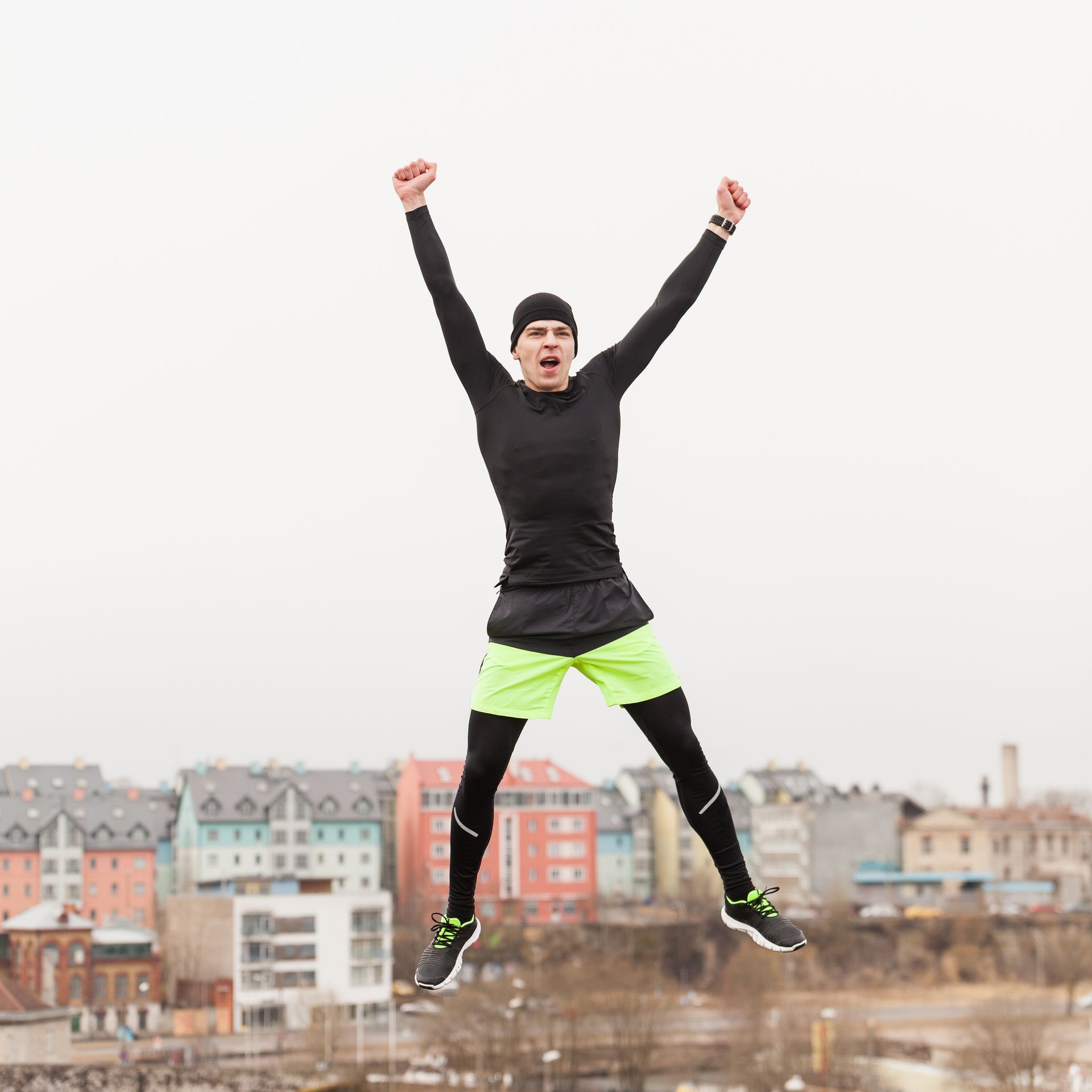 Man in athletic gear jumping, arms raised, with city background.