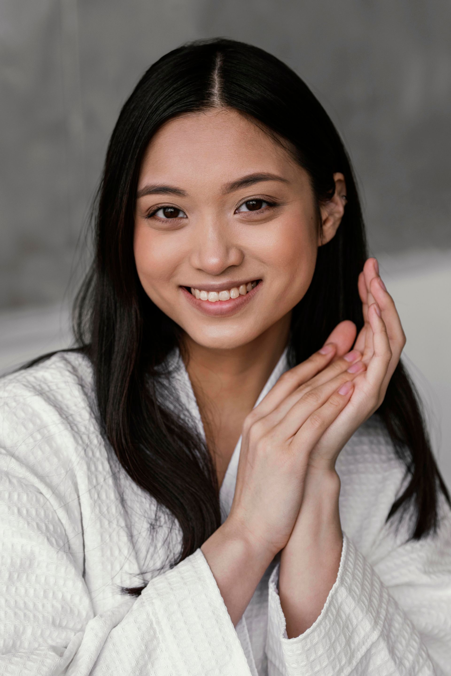 A woman in a white tank top is smiling with her hands on her chin.