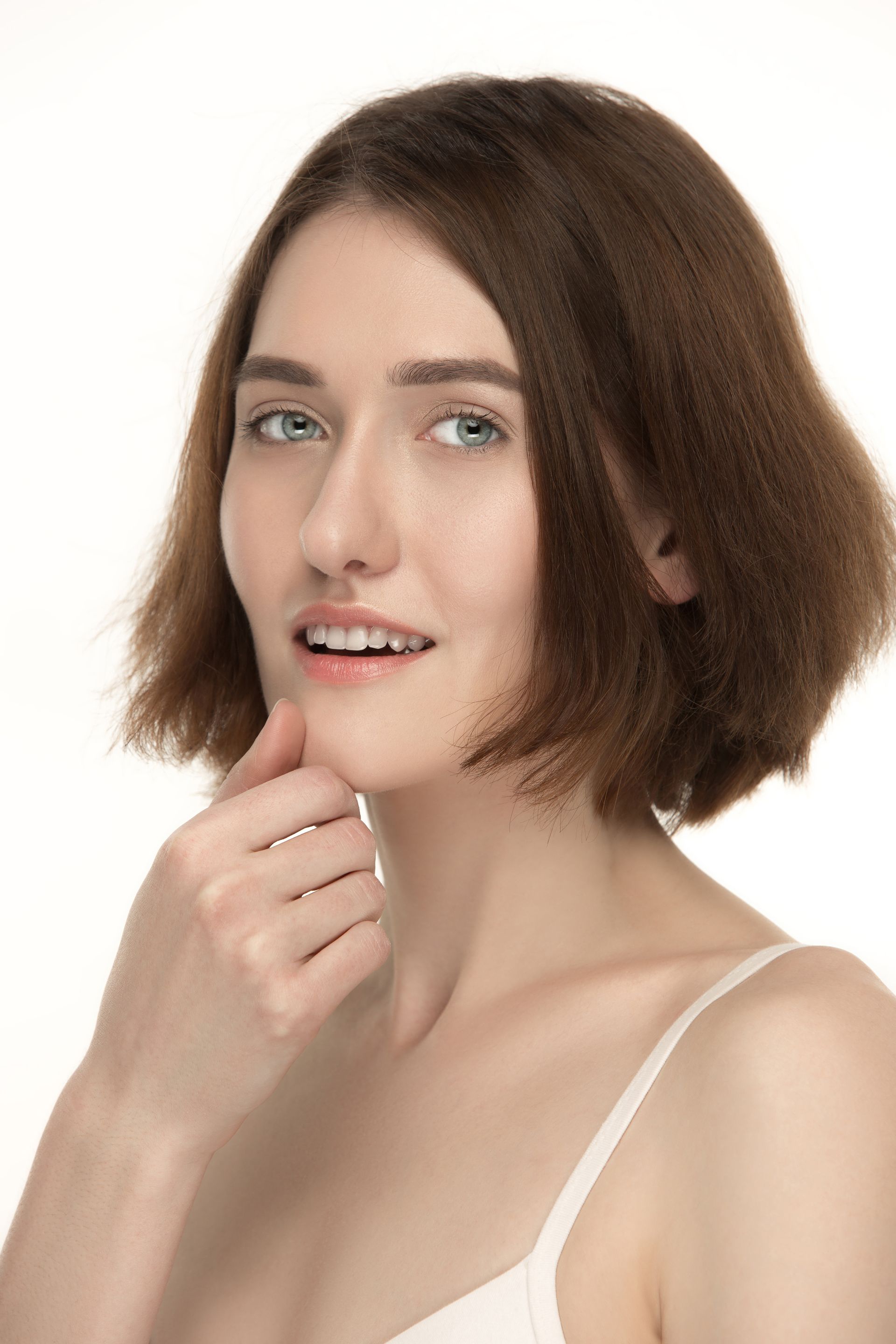 A woman in a white bra is smiling and touching her face.