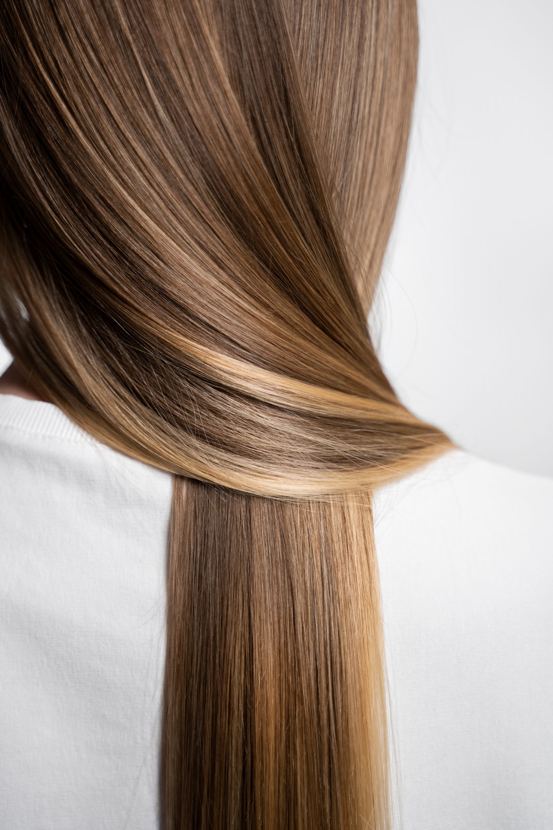 Woman's long brown and blonde hair cascading down her back over a white garment.