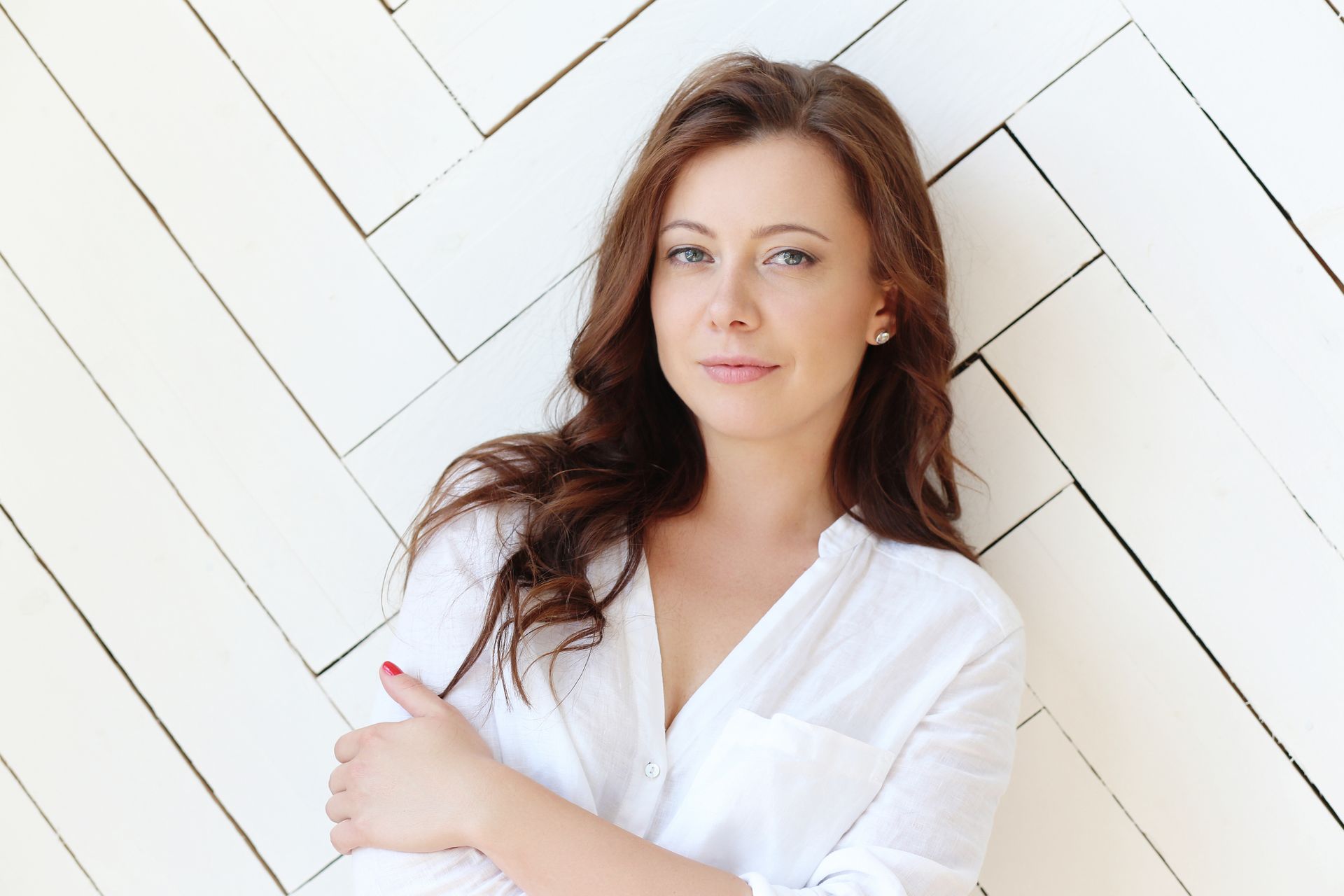 A woman in a white shirt is leaning against a white wall.