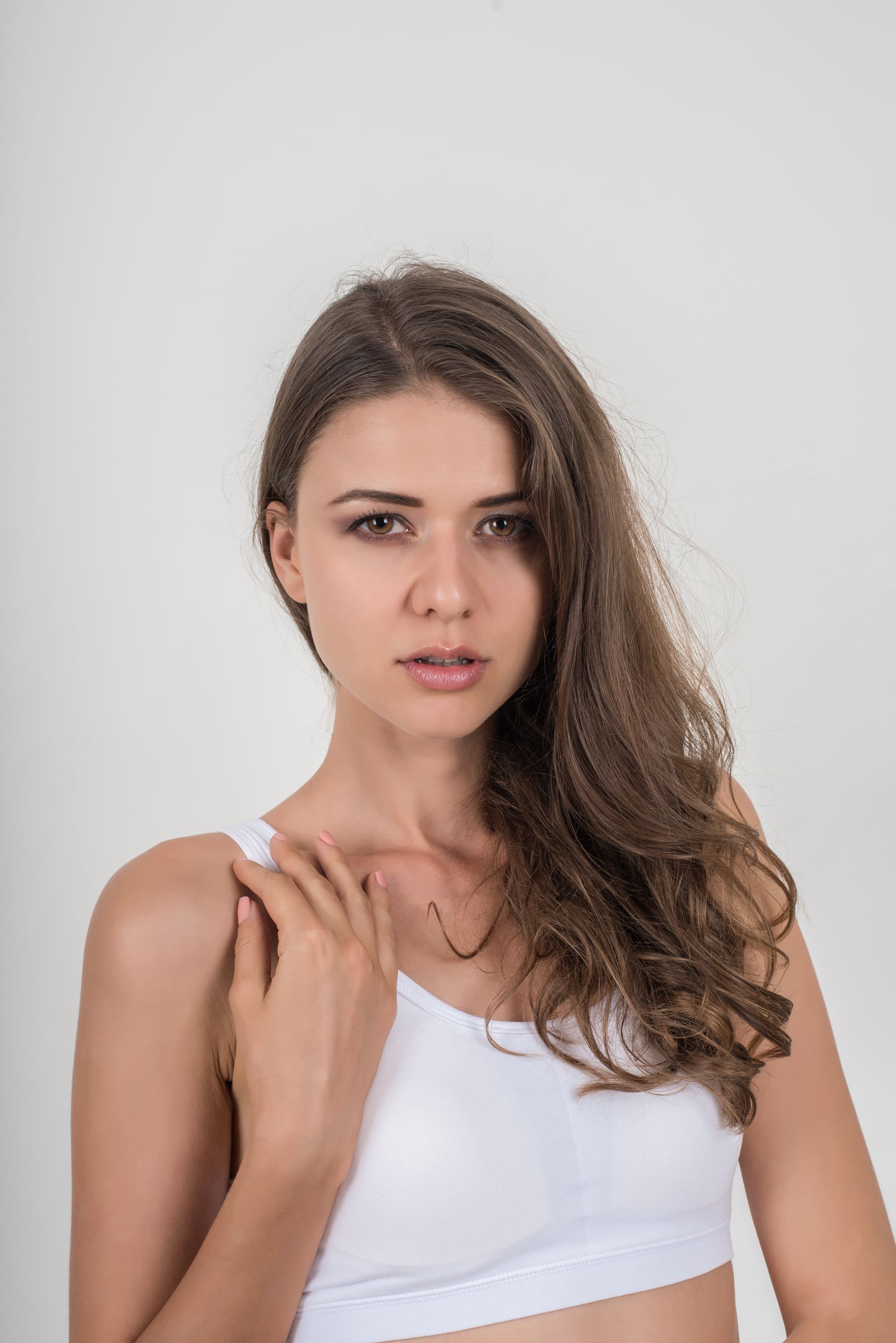 A woman in a white bra is standing in front of a white background.