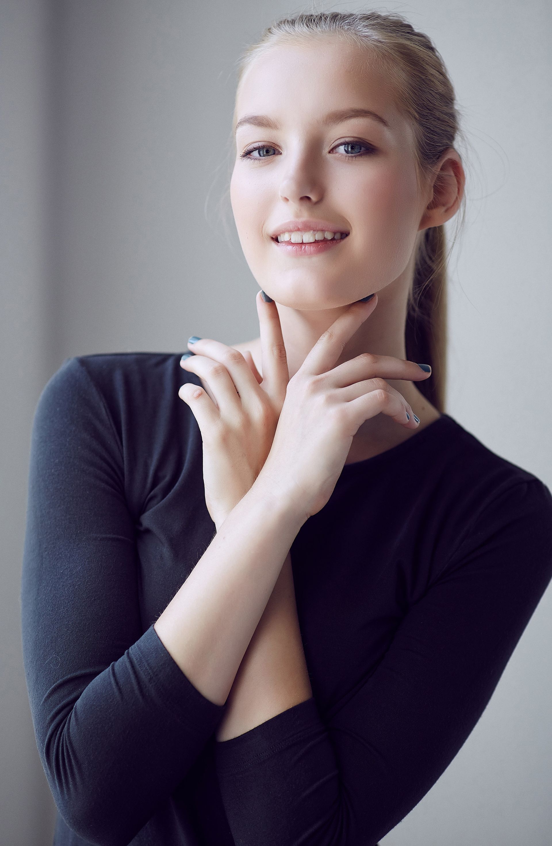 A woman in a black shirt is smiling with her hands on her face.