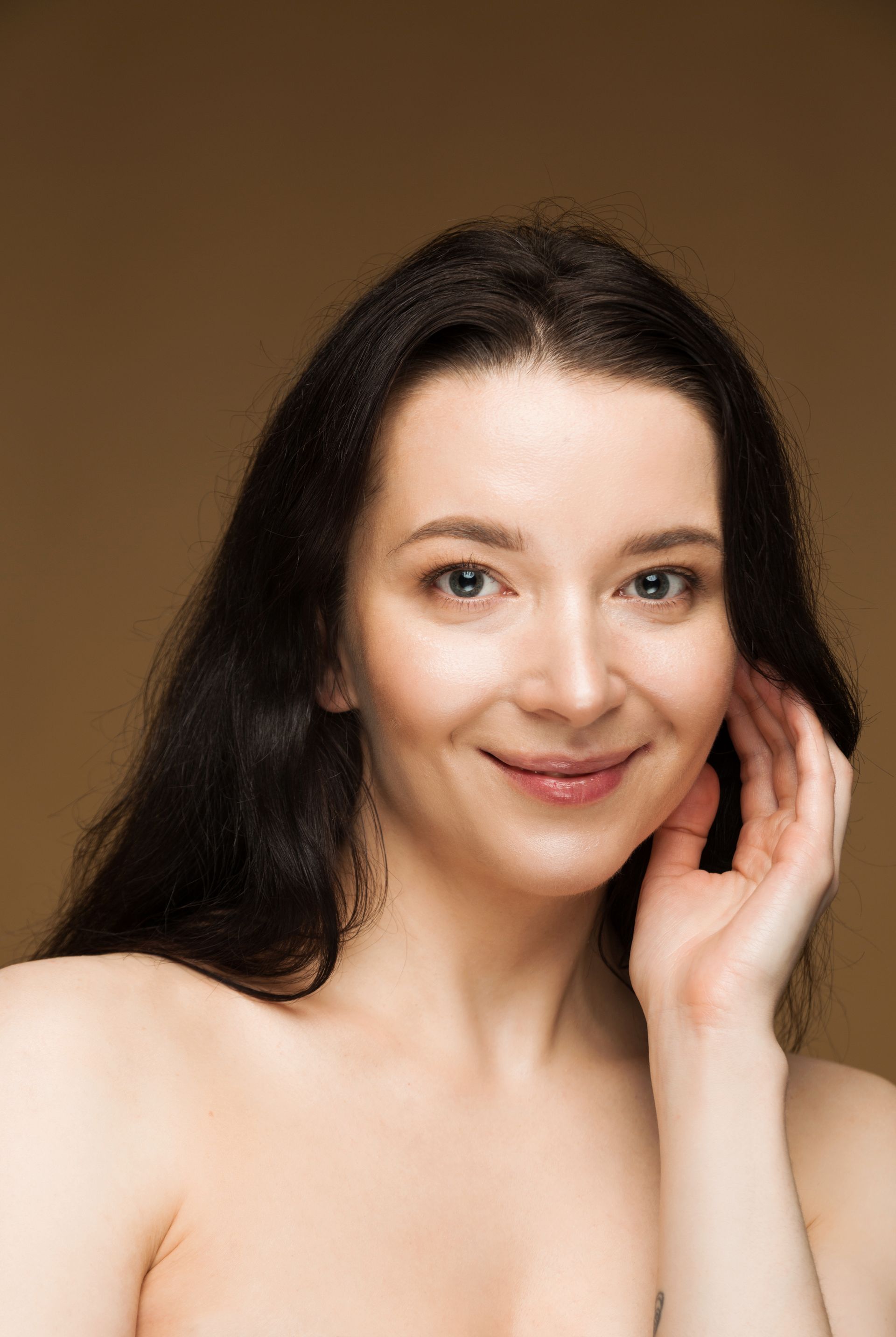 A woman is smiling and touching her face with her hand.