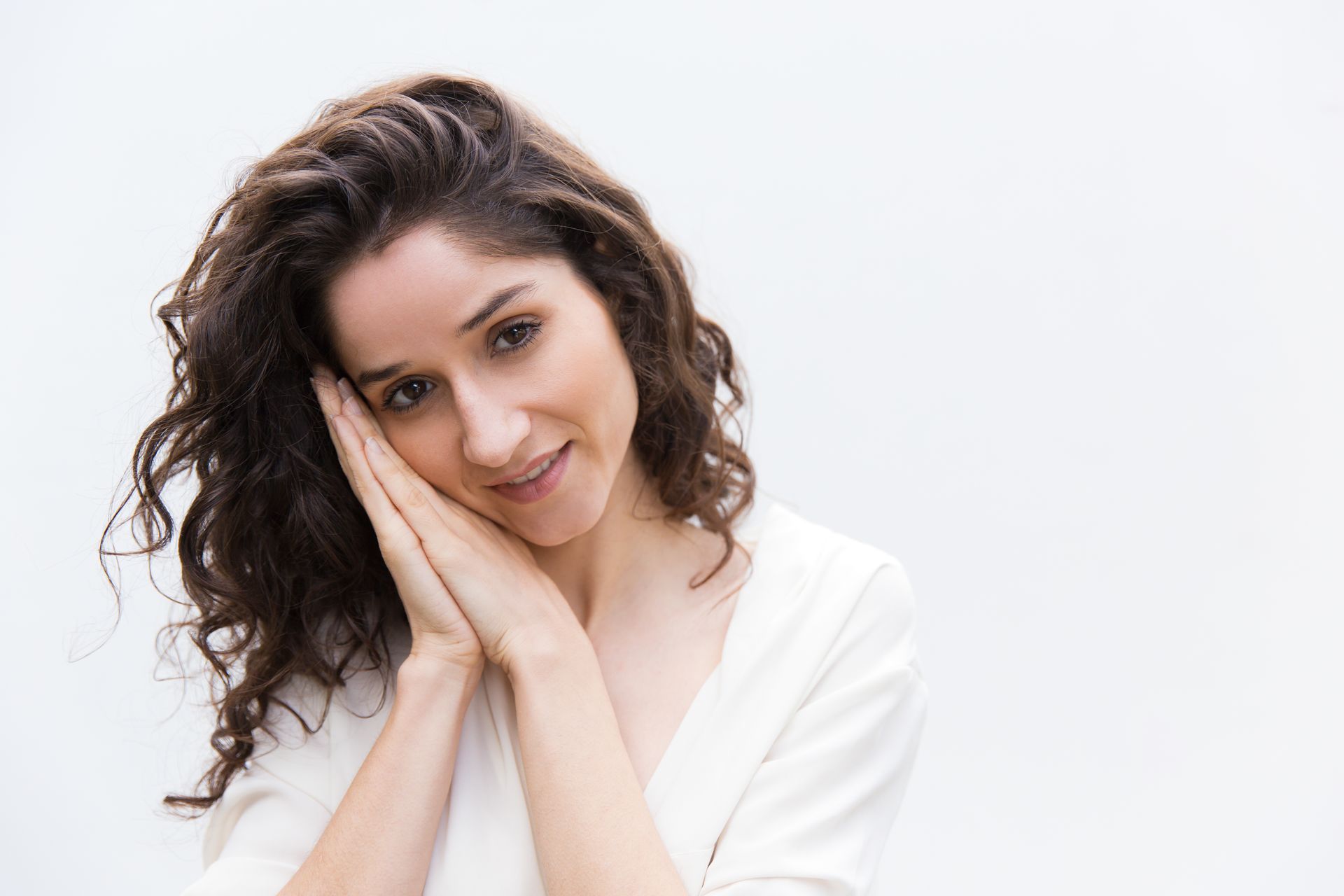 A woman with curly hair is smiling and holding her hand to her face.