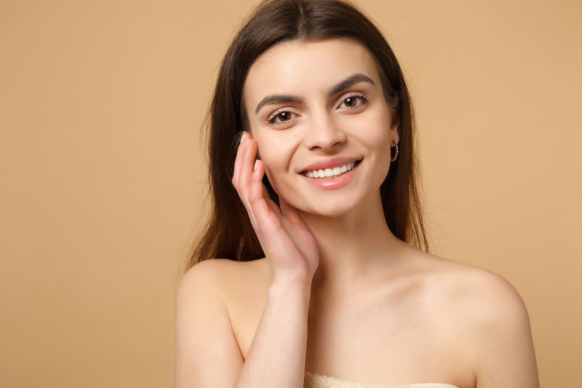 A woman is smiling and touching her face with her hand.