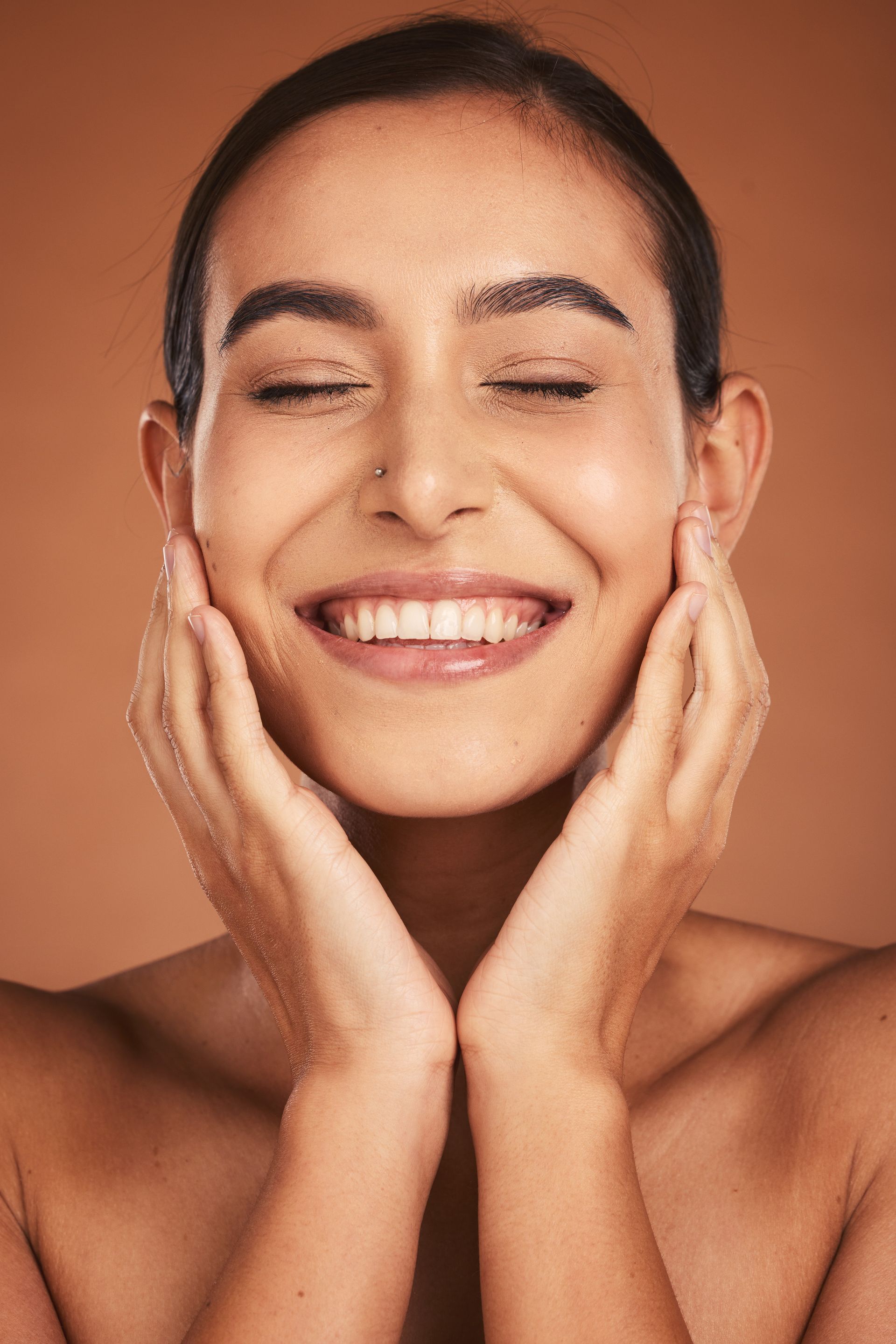 A woman is smiling and touching her face with her hands.