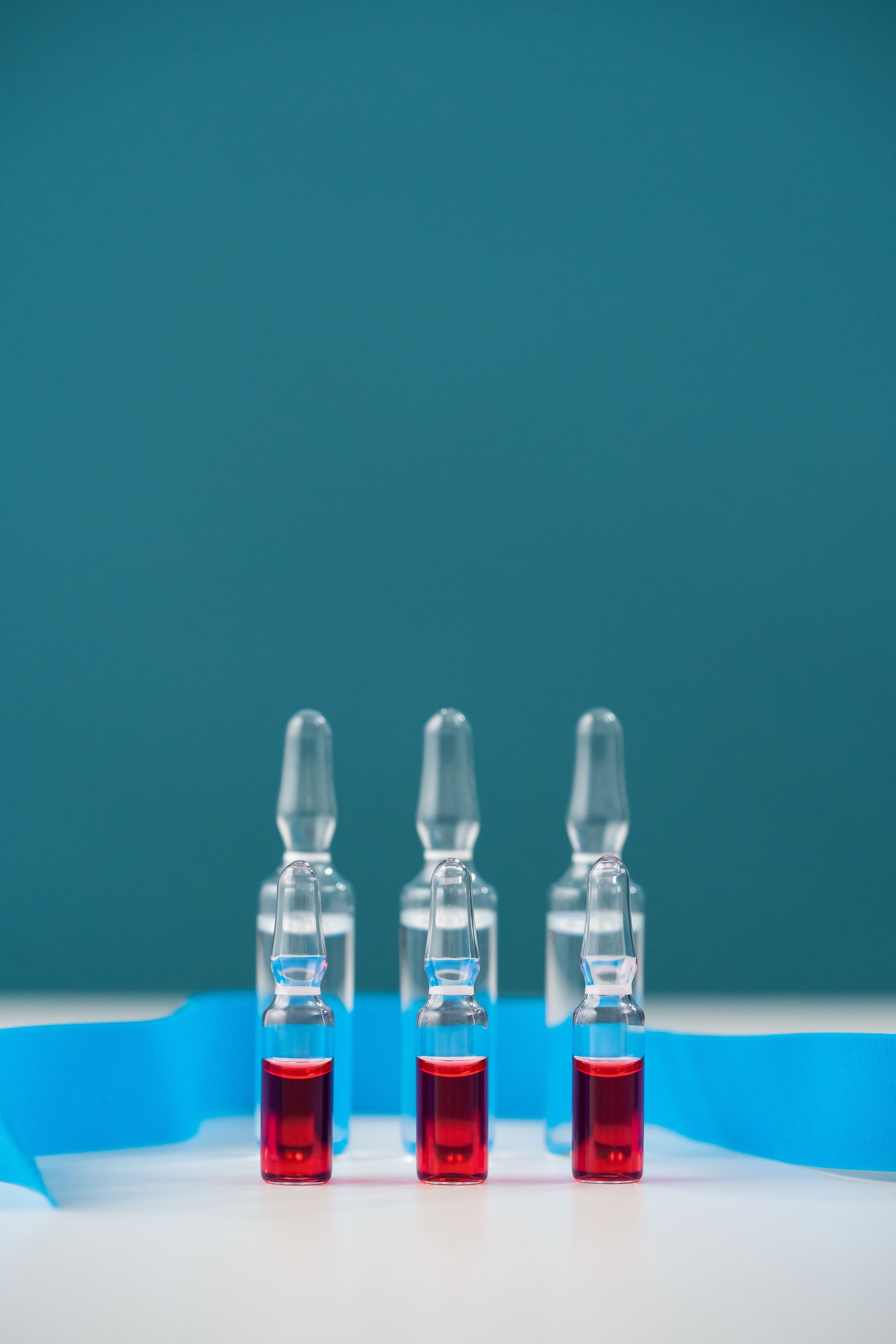 Three ampoules with red liquid are sitting on a table next to a blue ribbon.